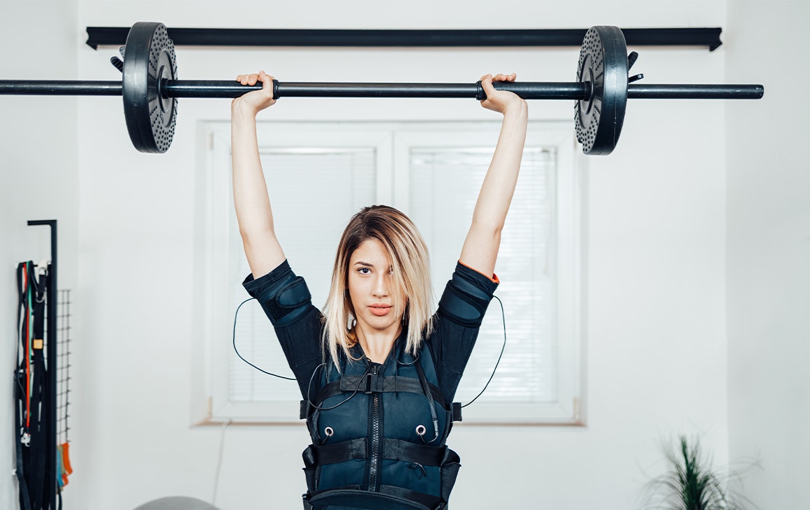 woman in an EMS training vest lifting a barbell